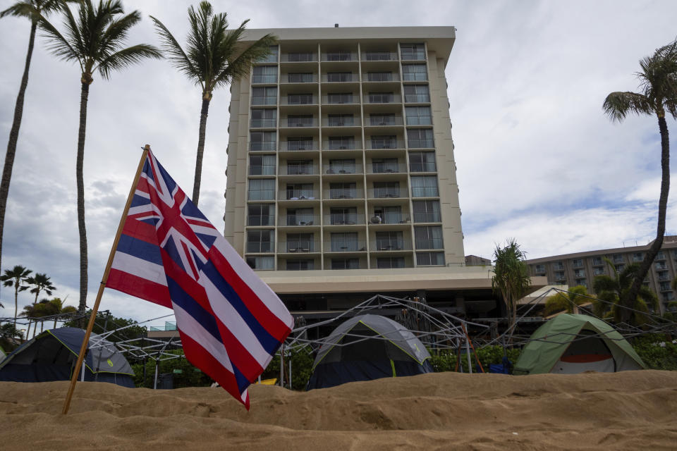 A resort looks over tents set up by Lahaina Strong for their "Fish-in" on Friday, Dec. 1, 2023, in Lahaina, Hawaii. Lahaina Strong has set up a "Fish-in" to protest living accommodations for those displaced by the Aug. 8, 2023 wildfire, the deadliest U.S. wildfire in more than a century. More than four months after the fire, tensions are growing between those who want to welcome tourists back to provide jobs and those who feel the town isn't ready for a return to tourism." (AP Photo/Ty O"Neil)