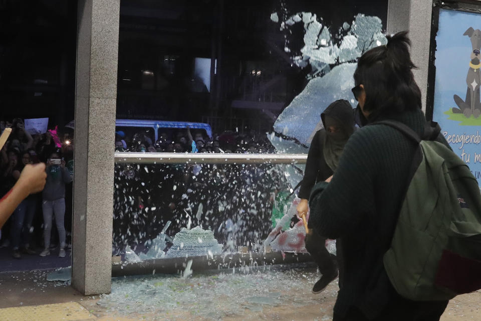 Una manifestante encapuchada rompe el vidrio de una estación de autobús al margen de una marcha de mujeres en Ciudad de México, el viernes 16 de agosto de 2019. (AP Foto/Marco Ugarte)