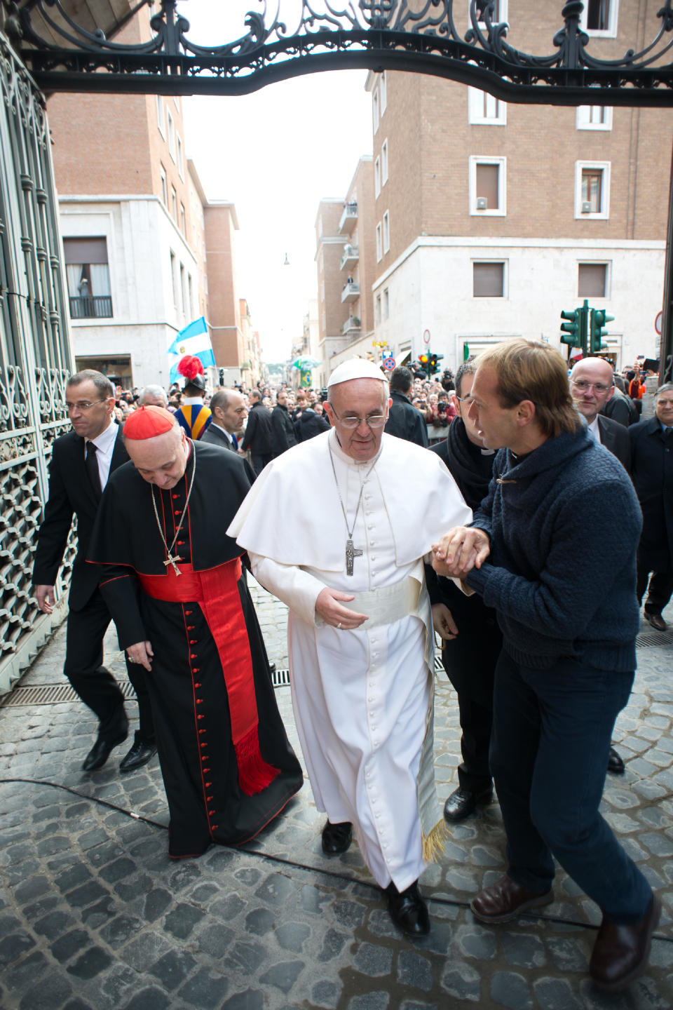 In this photo provided by the Vatican paper L'Osservatore Romano, Pope Francis enters a side gate of the Vatican after greeting a cheering crowd, Sunday, March 17, 2013. Pope Francis began his first Sunday as pontiff by making an impromptu appearance to the public from a side gate of the Vatican, startling passersby and prompting cheers, then kept up his simple, spontaneous style by delivering a brief, off-the-cuff homily at the Vatican's tiny parish church. Dressed only in white cassock, Francis waved to the crowd in the street outside St. Anna's Gate and before entering the church, which serves Vatican City State's hundreds of residents, he shook hands of the parishioners and kissed babies. (AP Photo/L'Osservatore Romano)