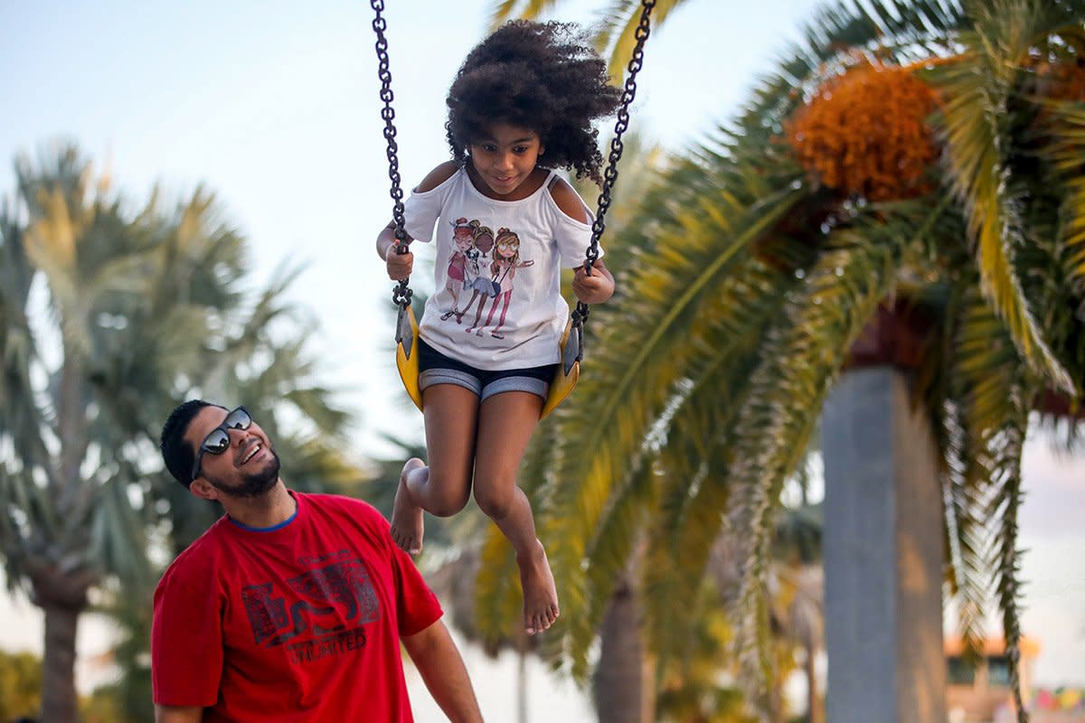 A father pushes his daughter on a swing.