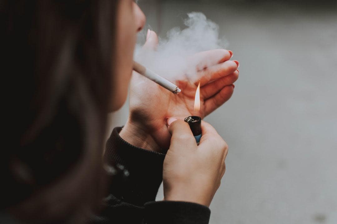 A woman lighting a cigarette and smoking with a puff of smoke. (Stock Image)