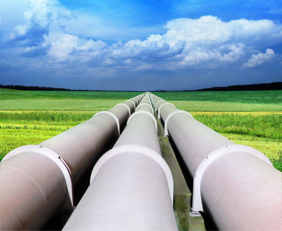 Three large pipelines in a green field heading towards a blue horizon.