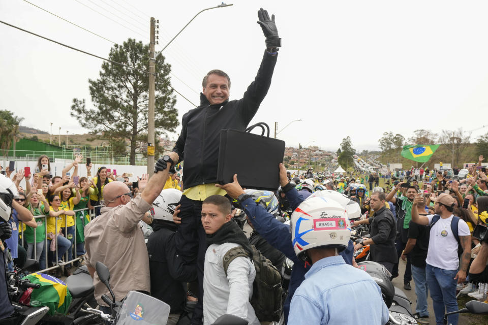 Brazilian President Jair Bolsonaro waves to supporters as he is surrounded by his security detail upon arrival to a motorcycle rally as he campaigns for a second term in Pocos de Caldas, Brazil, Friday, Sept. 30, 2022. Brazil's general elections are scheduled for Oct. 2. (AP Photo/Andre Penner)