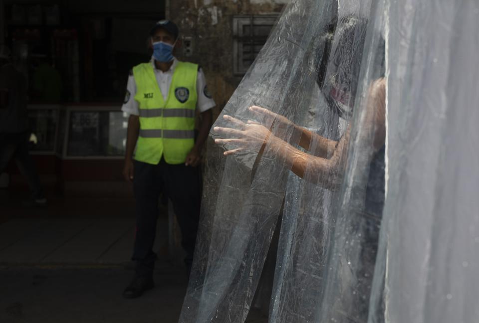 A woman wearing a protective face mask walks through a decontamination chamber as a preventive measure against the spread of the new coronavirus in the neighborhood of Petare in Caracas, Venezuela, Wednesday, July 15, 2020. (AP Photo/Ariana Cubillos)