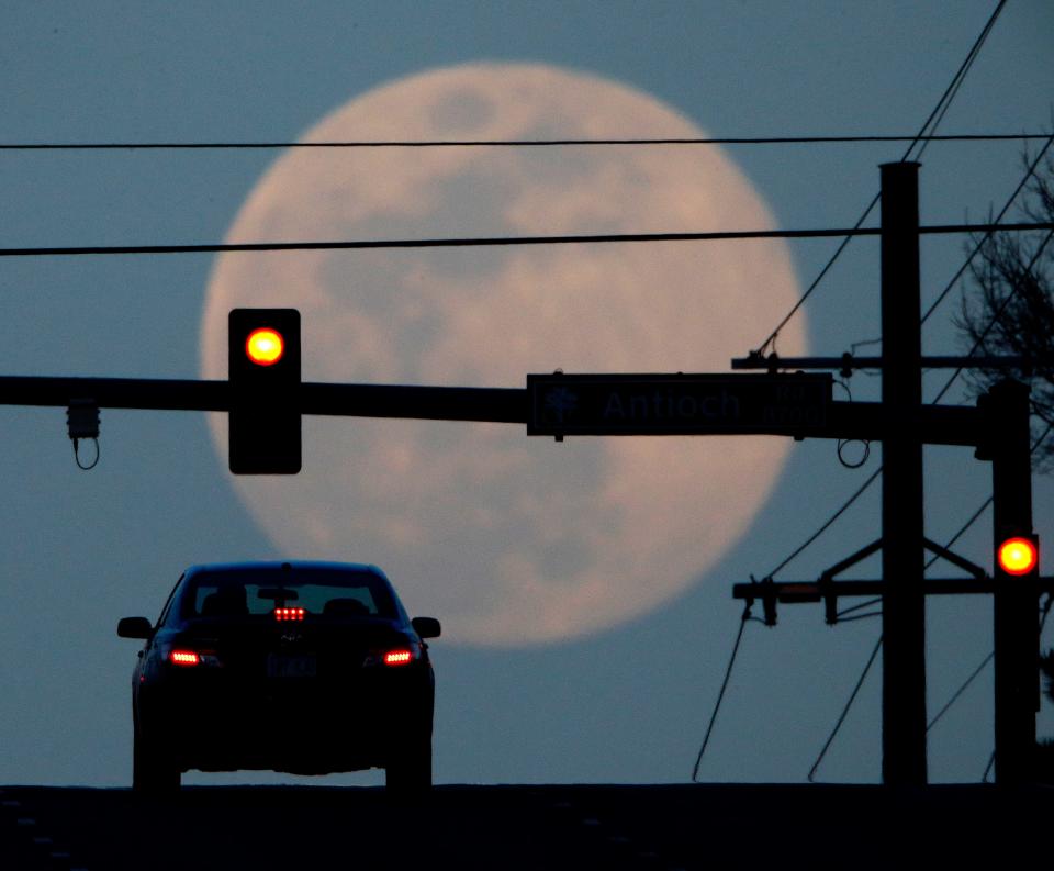 FILE - In this March 30, 2018, file photo, a motorist waits at a traffic light while the waxing full moon rises in the distance in Overland Park, Kan. The number of people killed by drivers running red lights has hit a 10-year high, and AAA is urging drivers and pedestrians to use caution at traffic signals. (AP Photo/Charlie Riedel, File)