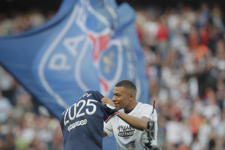 PSG's Kylian Mbappe waves a shirt to the crowd after it is announced that he has signed a three year extension to his deal to stay at the club ahead of the French League One soccer match between Paris Saint Germain and Metz at the Parc des Princes stadium in Paris, France, Saturday, May 21, 2022. (AP Photo/Michel Spingler)