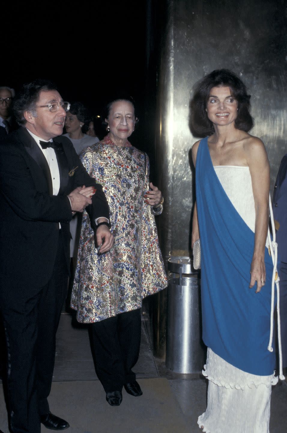 <p>Carl Katz, Diana Vreeland, and Jackie Onassis are photographed at the Metropolitan Museum of Art, with Jackie wearing a strapless white gown with a blue overlay. <br></p>