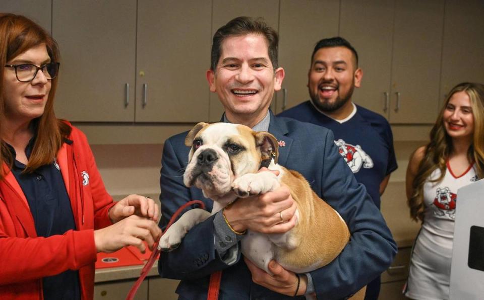 Fresno State President Dr. Saúl Jiménez-Sandoval, center, holds Victor E. Bulldog IV with caretaker Jacqui Glasener, left, and cheerleaders after the dog was introduced as Fresno State University’s newest live mascot during a press conference at the Smittcamp Alumni House at Fresno State on Tuesday, Nov. 29, 2022. Victor E Bulldog IV will officially take over for the retiring Victor E. Bulldog III during a changing of the collar ceremony in the spring.