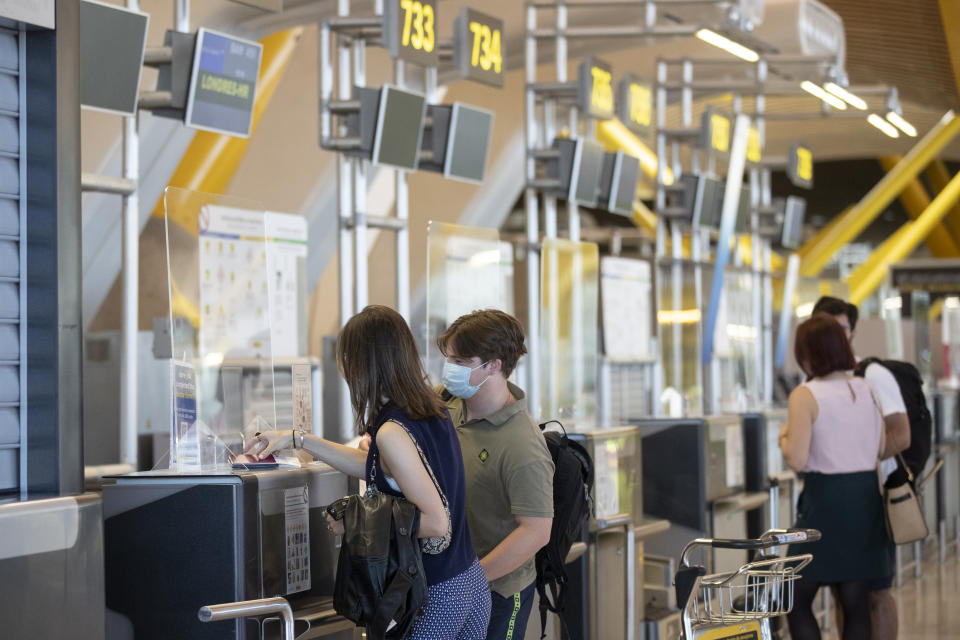 Passengers wearing face masks to prevent the spread of coronavirus check in prior to departure to London at a British Airways check-in desk at Adolfo Suarez-Barajas international airport, outskirts Madrid, Spain, Sunday, July 26, 2020. Britain has put Spain back on its unsafe list and announced Saturday that travelers arriving in the U.K. from Spain must now quarantine for 14 days. The move by the UK taken without forewarning has caught travelers off guard. (AP Photo/Manu Fernandez)