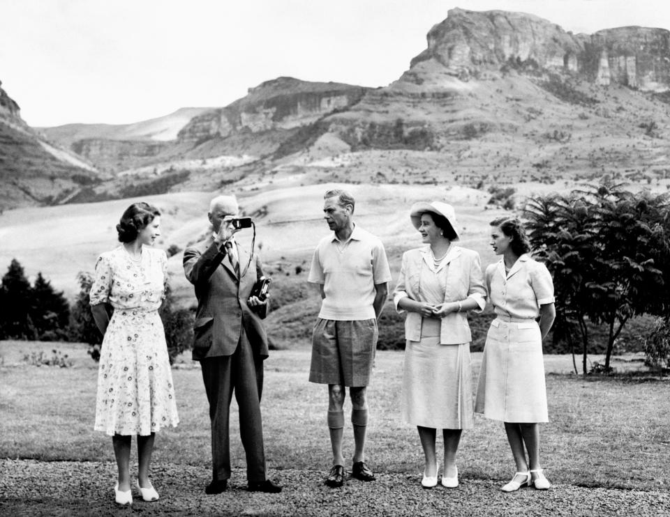 Five people stand in a row with mountain scenery in the background.