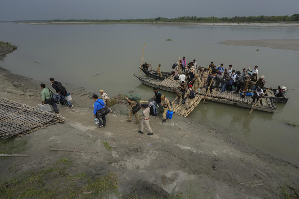 Polling officials carrying electronic voting machines and security personnel walk after disembarking from a boat after crossing the river Brahmaputra on the eve of parliament election at Baghmora Chapori (small island) of Majuli, India, April 18, 2024. (AP Photo/Anupam Nath)