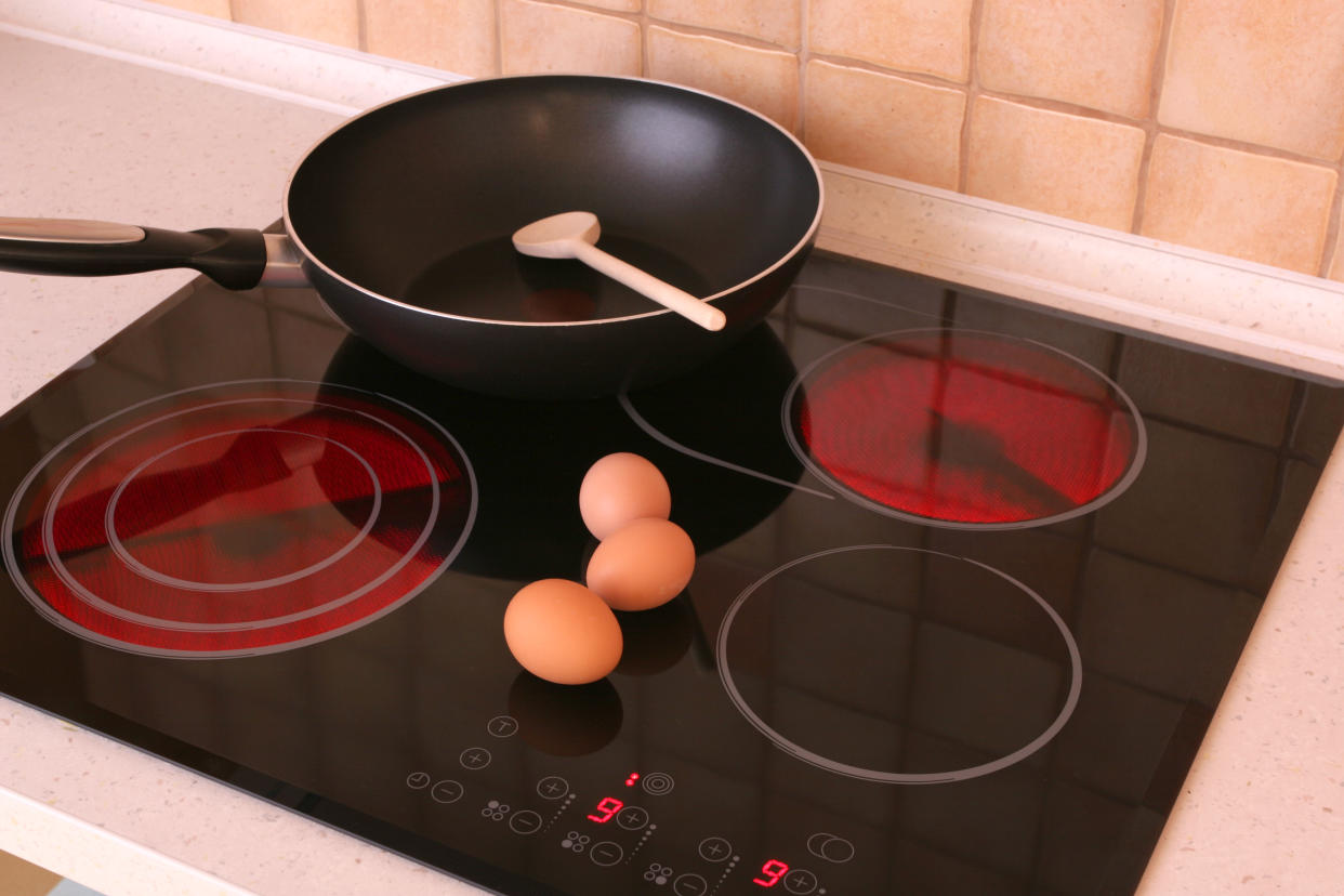 An electric stovetop with two burners lit, and a pan and three eggs on top of it. (Getty Images)