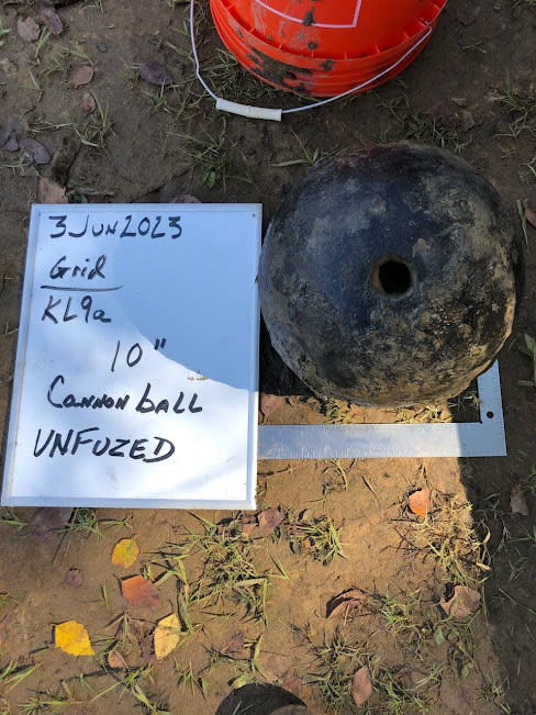 A cannonball rests on the muddy ground next to a red bucket and a whiteboard