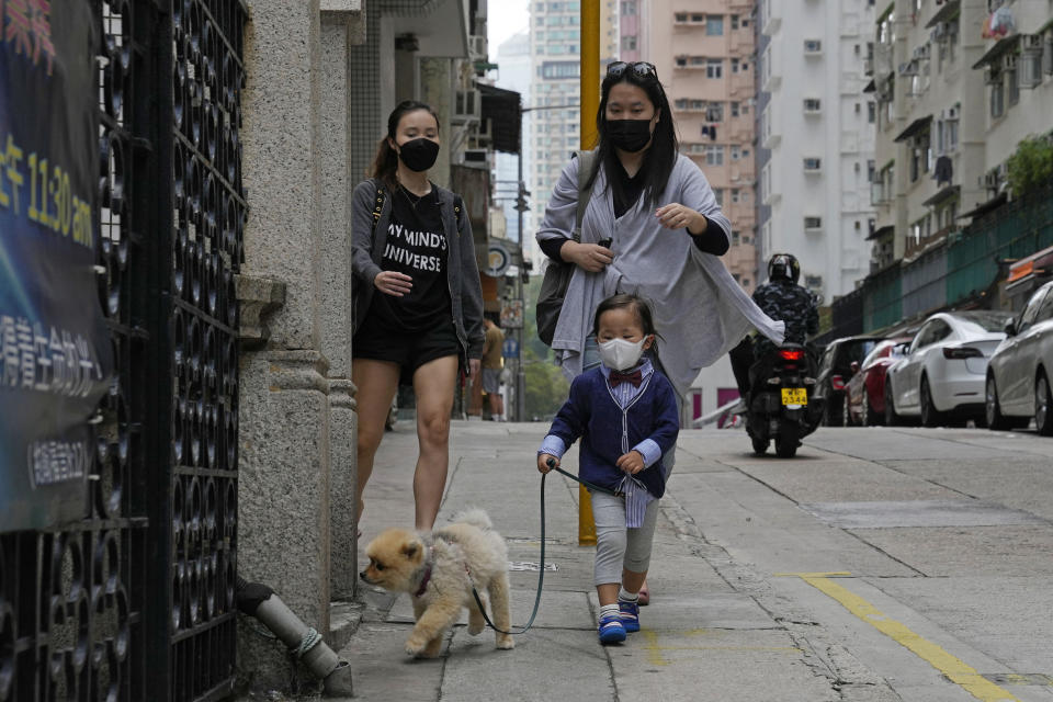 A child wearing a face mask walks a dog in Hong Kong, Sunday, March 13, 2022. The territory's leader, Chief Executive Carrie Lam, warned the peak of the latest surge in coronavirus infections might not have passed yet. (AP Photo/Kin Cheung)