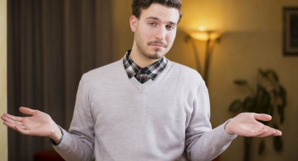 Confused or doubtful young man shrugging with palms open, indoor shot in a house