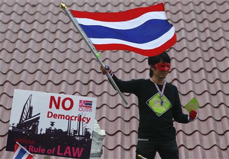 An anti-government protester waves a Thai national flag as he stands on a rooftop during a rally outside the Government House in Bangkok December 9, 2013. REUTERS/Chaiwat Subprasom