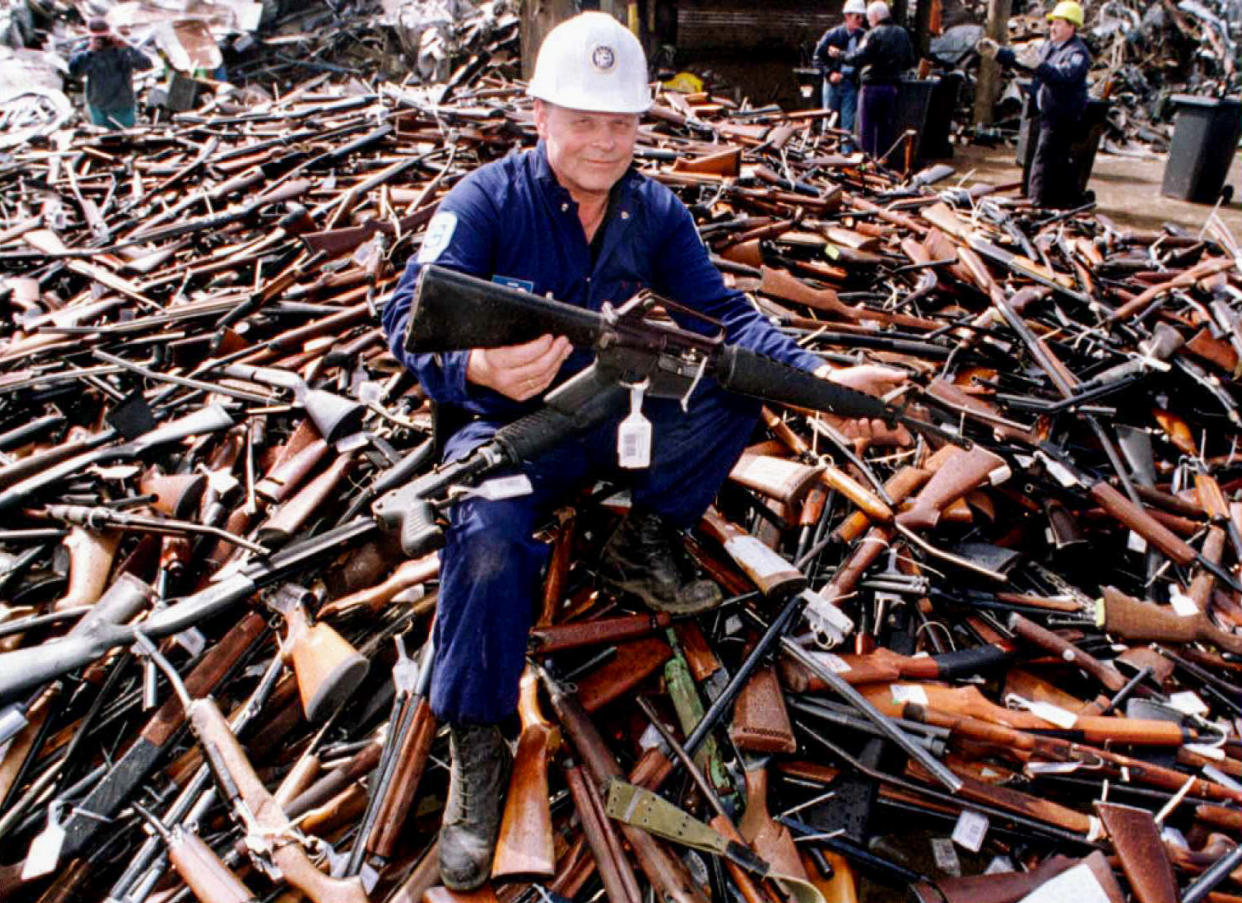 Seated on a pile of weapons, security firm project supervisor Norm Legg holds up an Armalite rifle, similar to the one used in the Port Arthur massacre, Melbourne, Victoria, Australia, on Sept. 8, 1996. (William West / AFP via Getty Images file)