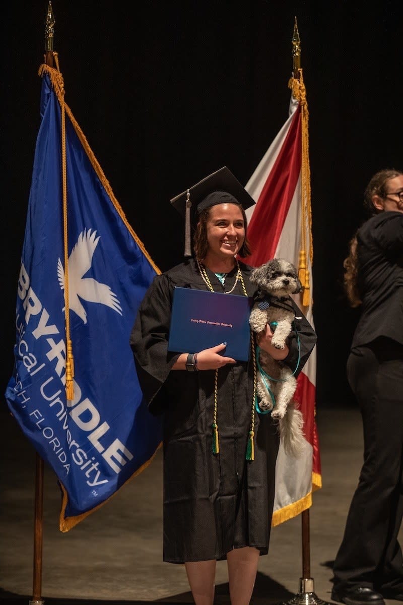 College graduate holding service dog and posing for picture with diploma