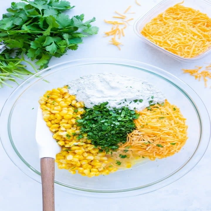 Corn, cheese, cilantro, and ingredients for fritters in a bowl.