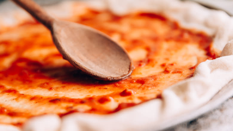 Spreading pasta sauce on pizza