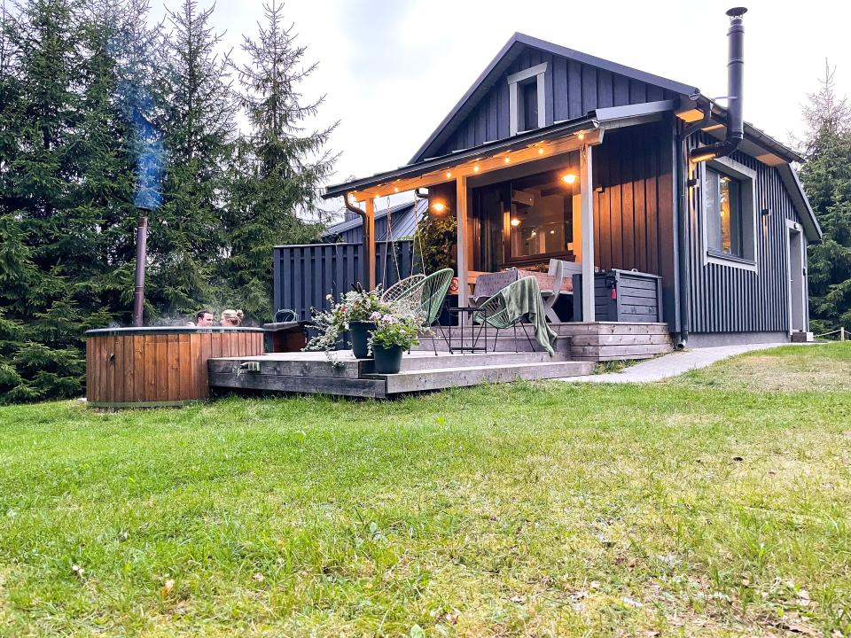 A house in the woods with a hot tub and two people inside.