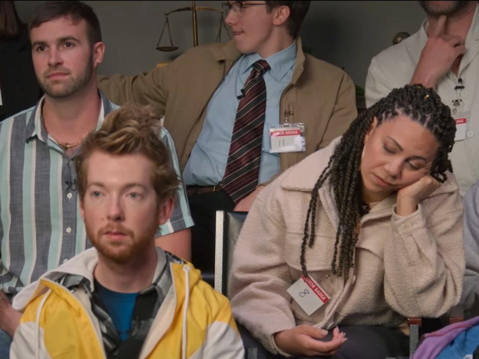 Cast of "Jury Duty" sitting in chairs. One woman is holding her head up and appears to be sleeping