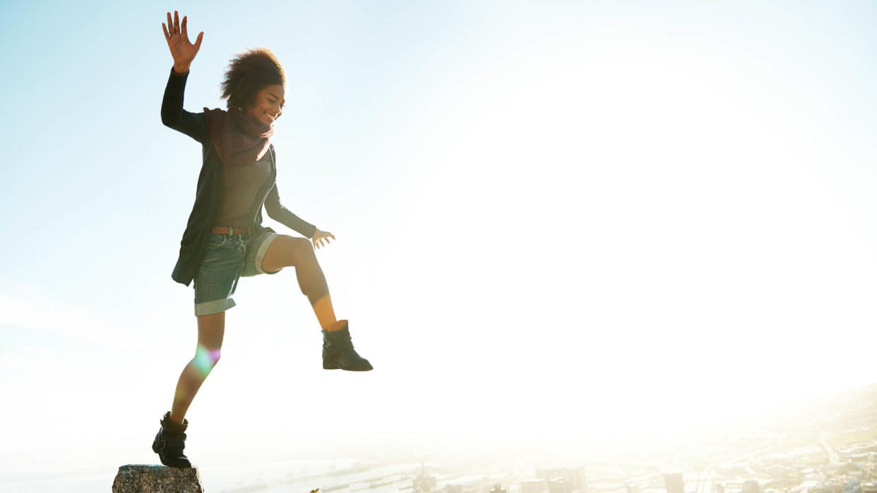 Shot of a young woman jumping from pillar to pillar on the edge of a mountain road.