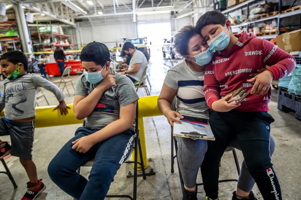 Indira Cisneron holds her son German Vazquez while waiting to get her first COVID-19 vaccine shot as her other son Gabriel Vasquez, left, 13,  waits in southwest Detroit.