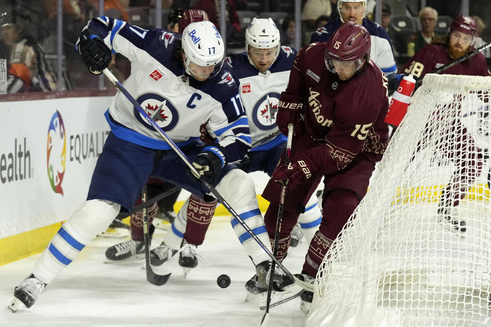 Winnipeg Jets center Adam Lowry (17) battles with Arizona Coyotes center Alexander Kerfoot (15) for the puck as Jets defenseman Neal Pionk (4) looks on during the first period of an NHL hockey game Saturday, Nov. 4, 2023, in Tempe, Ariz. (AP Photo/Ross D. Franklin)