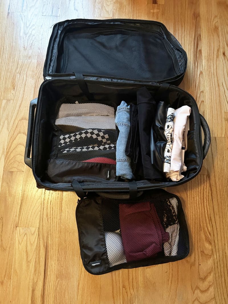 Suitcase on floor  packed with rolled clothes and mesh bag on side