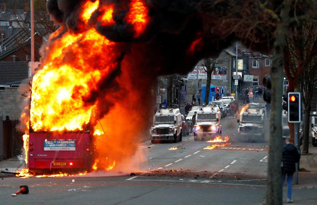 Police vehicles are seen behind a hijacked bus burns on the Shankill Road as protests continue in Belfast, Northern Ireland, April 7.