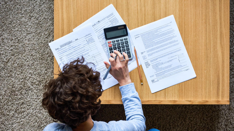 High angle view of busy woman using calculator while doing paperwork at home.