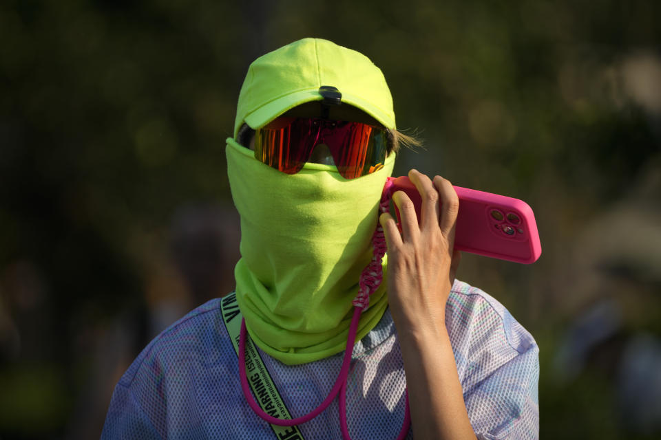 A man wearing a face cover uses his mobile phone as he walks during an unseasonably hot day in Beijing, Sunday, June 16, 2024. China is being buffeted by two weather extremes, with heavy rain and flooding in parts of the south and a heat wave and potential drought in the north. (AP Photo/Andy Wong)