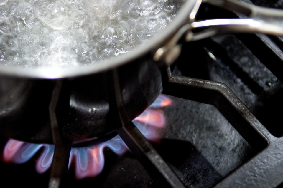 A pot of boiling water sits on a burner of a gas stove. 