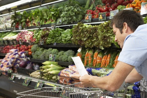 Young man reading shopping list in produce aisle, side view, close-up