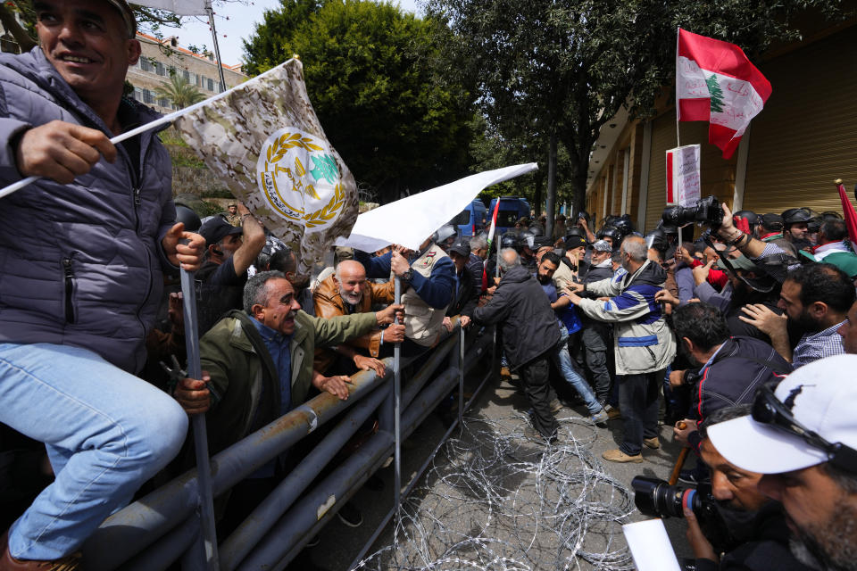 Retired members of the Lebanese security and other protesters try to remove barbed-wire barrier and a gate in order to advance towards the government building, background, during a protest demanding better pay in Beirut, Lebanon, Wednesday, March 22, 2023. Lebanese security forces fired tear gas to disperse hundreds of protesters who tried to break through the fence leading to the government headquarters in downtown Beirut Wednesday amid widespread anger over the harsh economic conditions in the country. (AP Photo/Hassan Ammar)