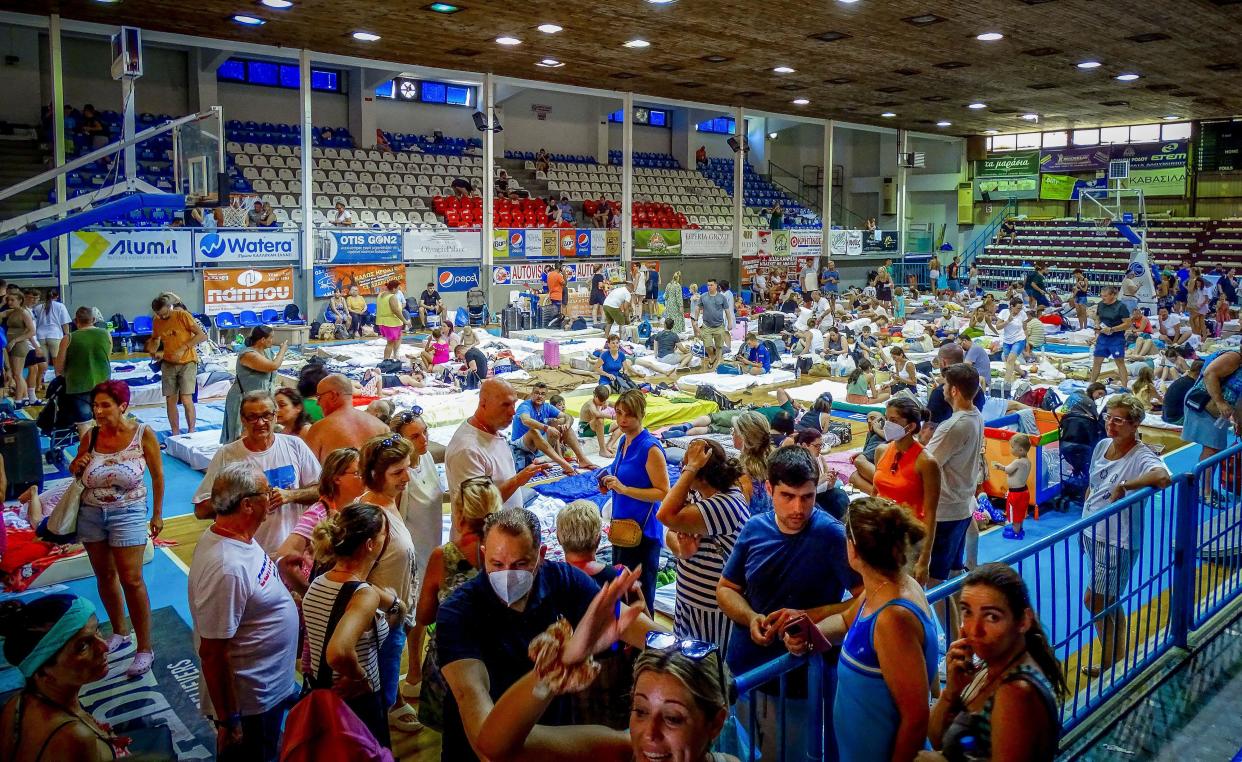 Evacuees sit inside a stadium following their evacuation during a forest fire on the island of Rhodes, Greece, Sunday, July 23, 2023. Some 19,000 people have been evacuated from the Greek island of Rhodes as wildfires continued burning for a sixth day on three fronts, Greek authorities said on Sunday. (Argyris Mantikos/Eurokinissi via AP)