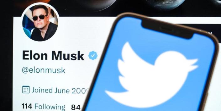 In this photo illustration, the Twitter logo is displayed on the screen of the phone, with Elon Musk's Twitter account in the background.