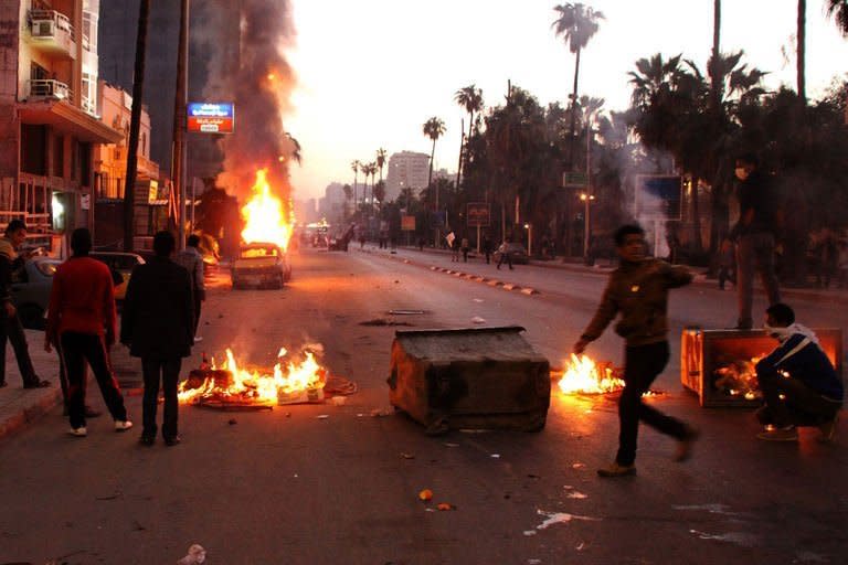 Egyptian anti-government protesters take cover behind burning bins during clashes with riot police, in the northern coastal city of Alexandria, on February 8, 2013. More than 120 people were injured in unrest across Egypt on Friday