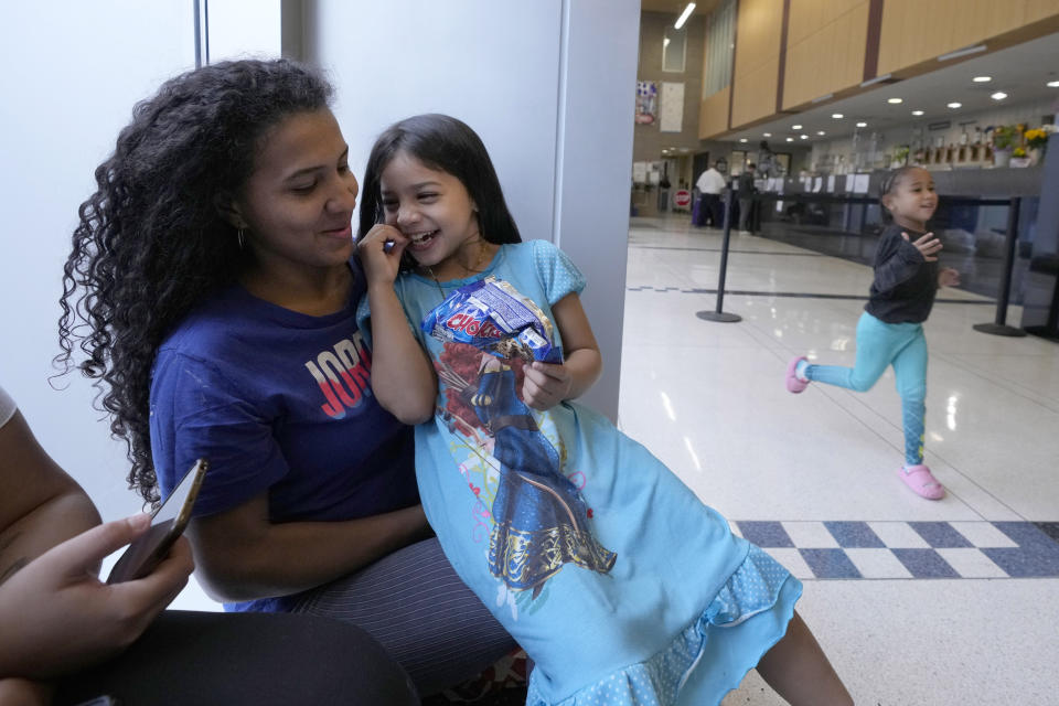 Karen Malave, left, an immigrant from Venezuela, and her daughter, Avril Brandelli, smile as Charlotte runs past them while they take shelter in the Chicago Police Department's 16th District station Monday, May 1, 2023. Chicago has seen the number of new arrivals grow tenfold in recent days. Shelter space is scarce and migrants awaiting a bed are sleeping on floors in police stations and airports. (AP Photo/Charles Rex Arbogast)