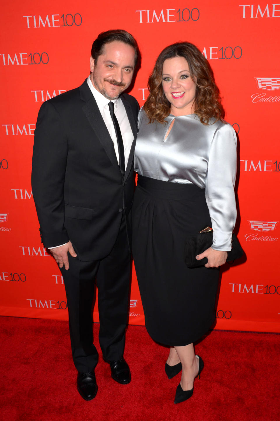 Melissa McCarthy, wearing a fancy work outfit, with husband Ben Falcone in a classic tuxedo