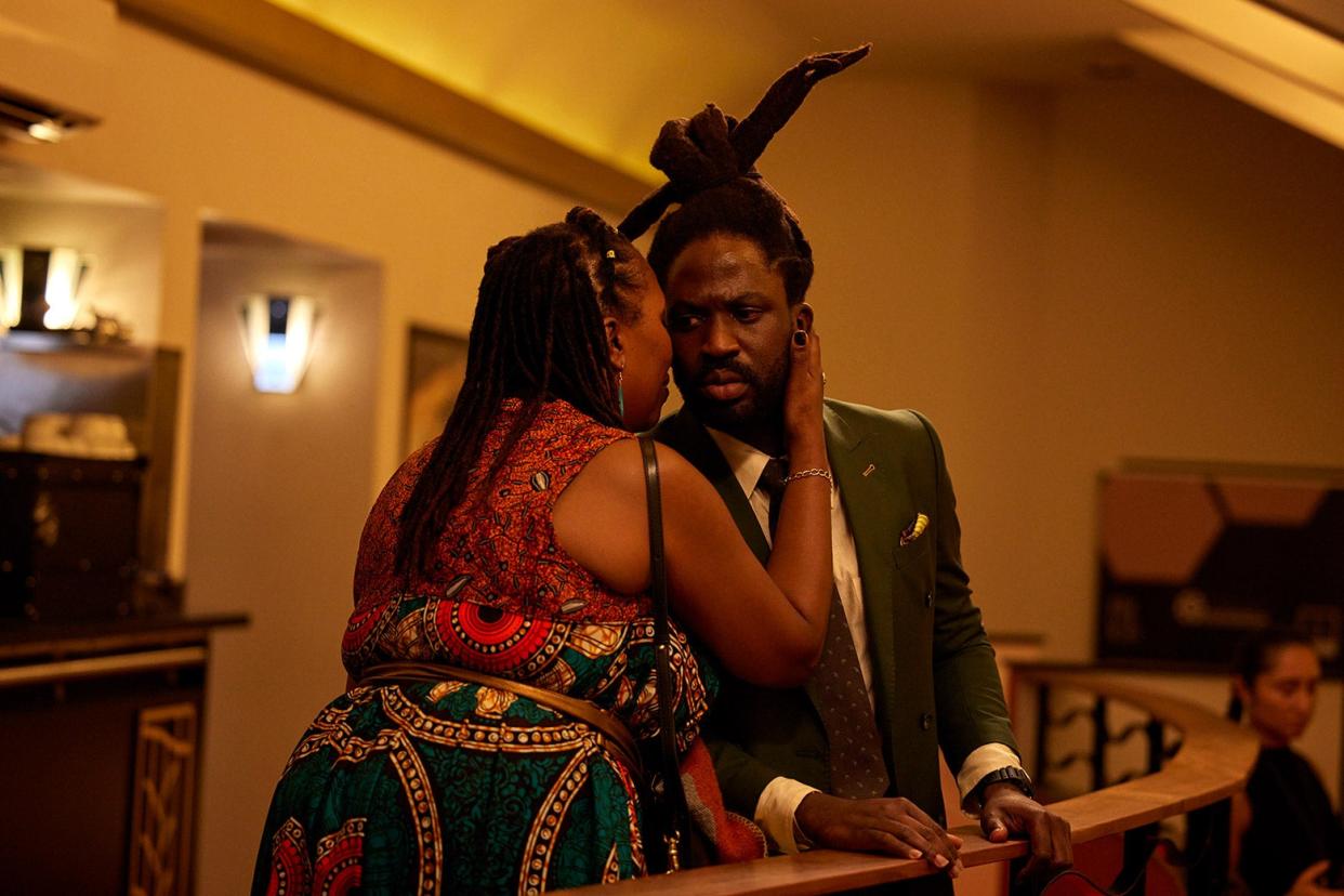 Kwabena dressed in a suit, with his mother hugging him, on a stair landing.