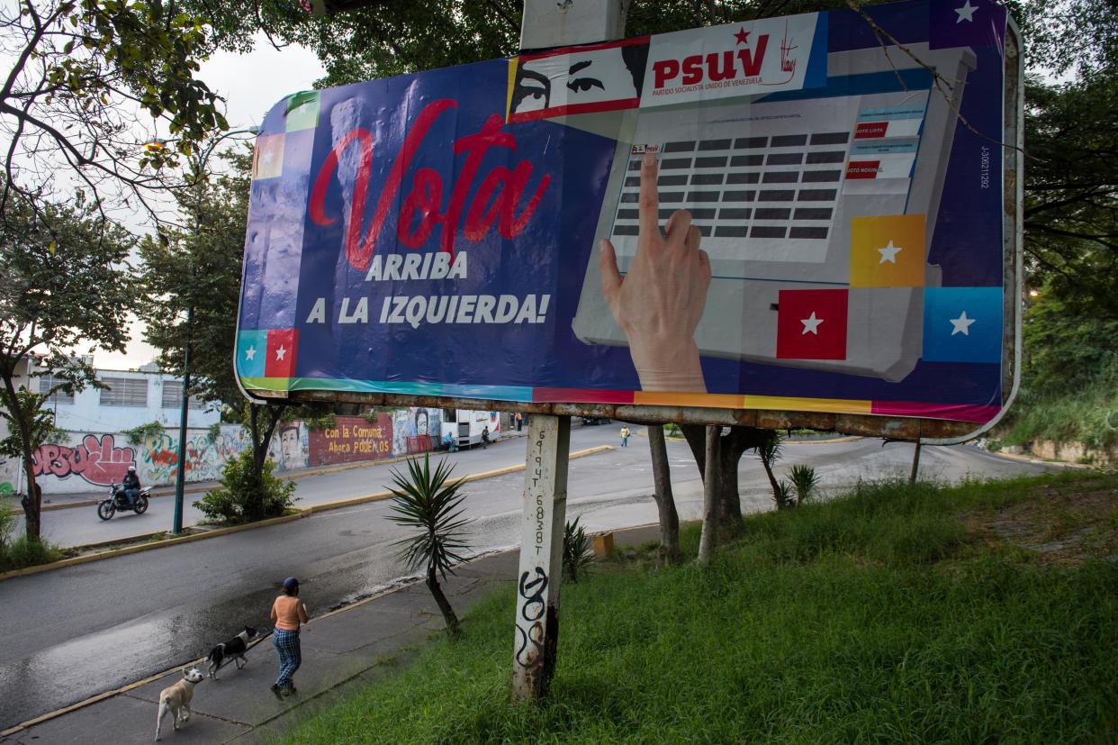 People walk near political propaganda depicting the eyes of late Venezuelan President Hugo Chavez, in Caracas on December 2, 2020 ahead of parliamentary elections in the country. - Venezuelan will hold legislative elections on December 6. (Photo by Cristian Hernandez / AFP) (Photo by CRISTIAN HERNANDEZ/AFP via Getty Images)