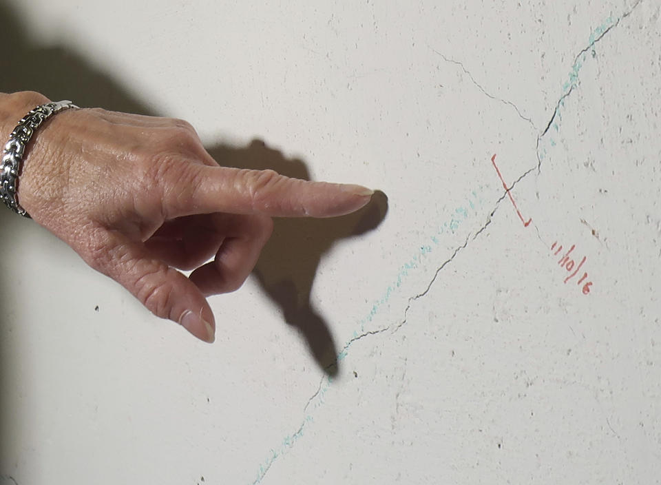 In this July 1, 2019 photo, Wendy Padula points to a crack in the crumbling foundation of her home in Vernon, Conn. She marks and dates the cracks when she discovers them to document the decay. The foundation of her home is deteriorating due to the presence of an iron sulfide known as pyrrhotite, often described as "a slow-moving disaster," which causes concrete to crack and break gradually as it becomes exposed to water and oxygen. After worrying for years about the foundations crumbling beneath their houses, hundreds of suburban homeowners in a large swath of eastern Connecticut are getting help from the state to salvage their properties that had been doomed by bad batches of concrete. (AP Photo/Ted Shaffrey)