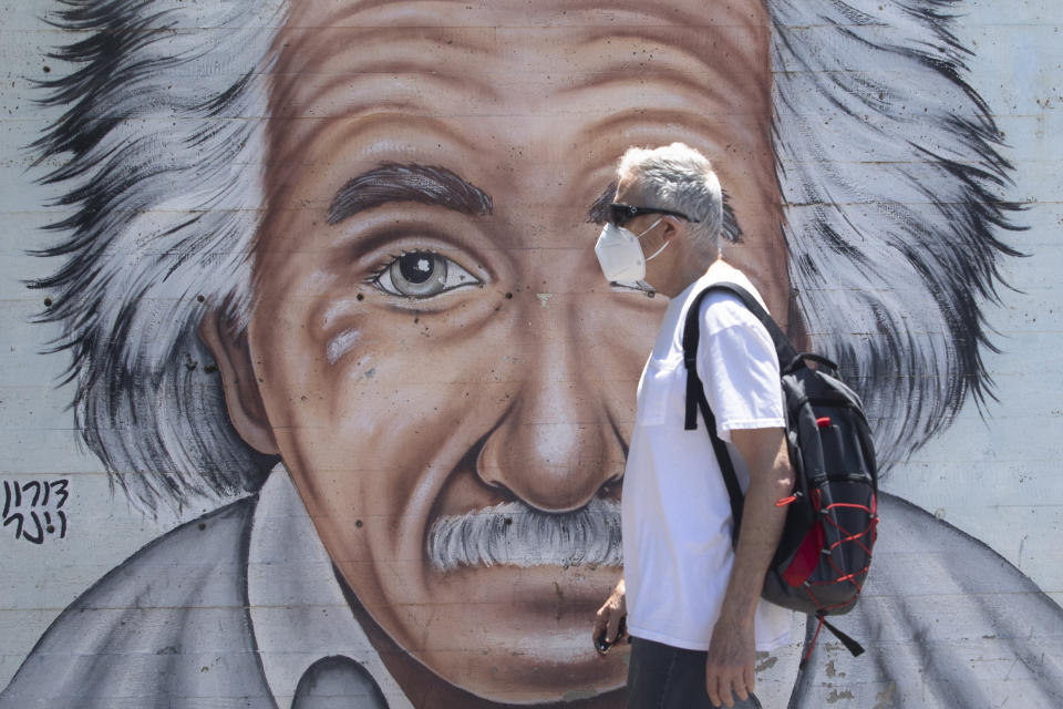 An Israeli man wearing a mask to curb the spread of the coronavirus walks past a mural showing Albert Einstein in Tel Aviv, Israel, Wednesday, July 15, 2020. (AP Photo/Sebastian Scheiner)