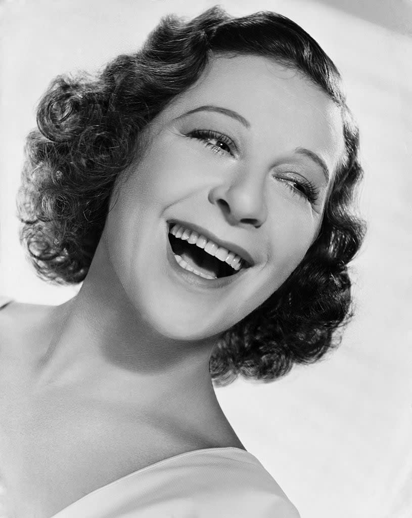 A smiling woman with short, curly hair in a classic portrait poses. The person's identity is unknown