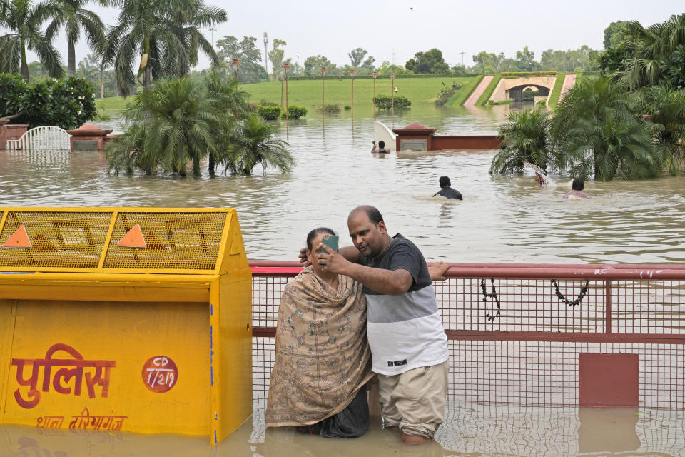 A couple takes a selfie in front of Rajghat, a memorial dedicated to Mahatma Gandhi, standing in floodwaters from the river Yamuna in New Delhi, India, Friday, July 14, 2023. (AP Photo/Manish Swarup)