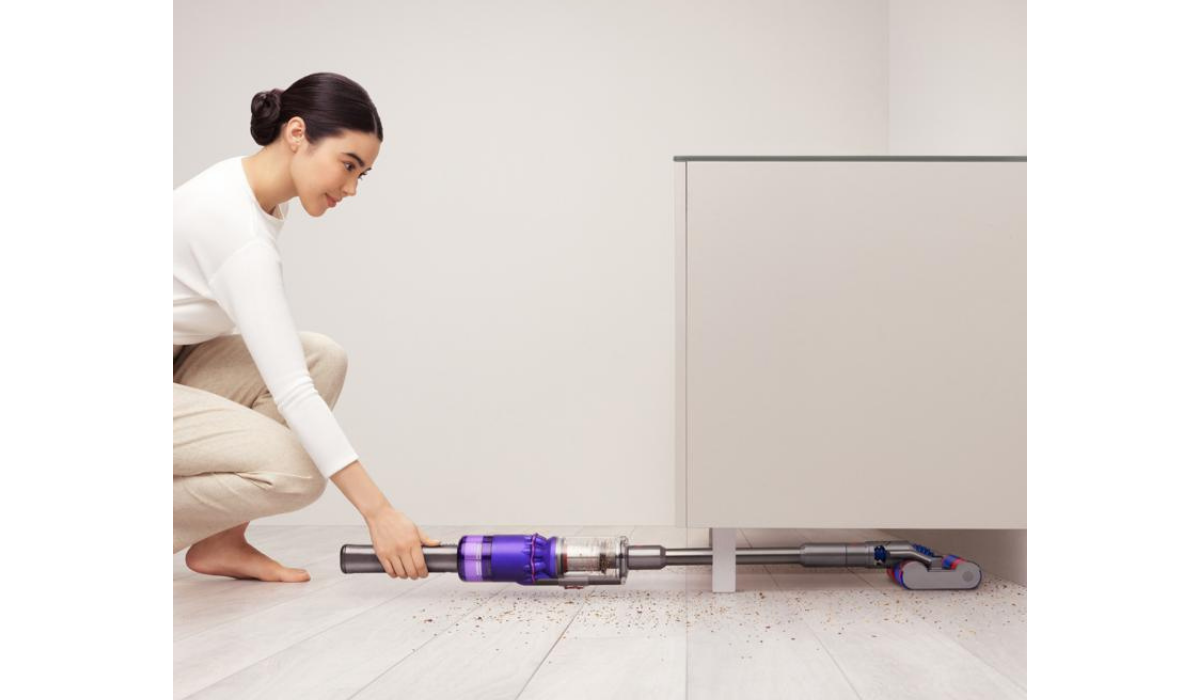 Woman using vacuum flat against the floor to reach under furniture. 