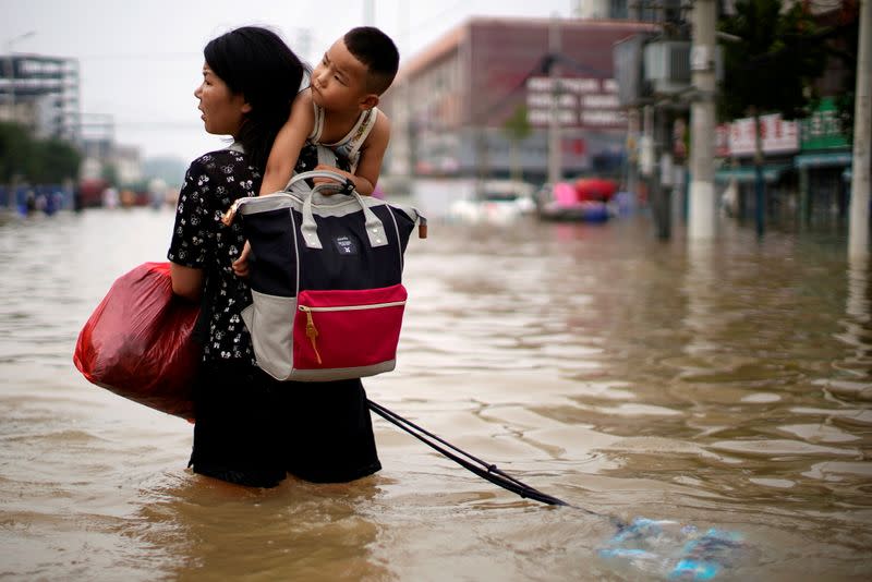 FILE PHOTO: Woman carrying a child and belongings wades through floodwaters following heavy rainfall in Zhengzhou