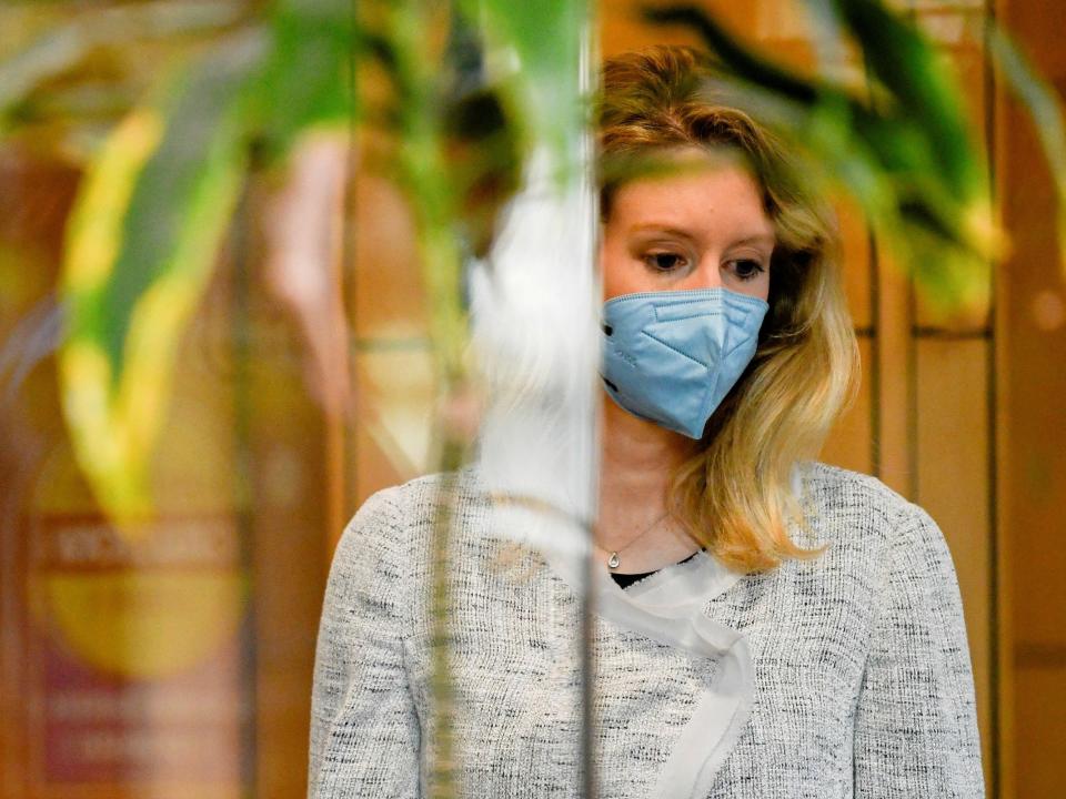 Theranos founder Elizabeth Holmes is seen wearing a blue mask and gray sweater in a courthouse